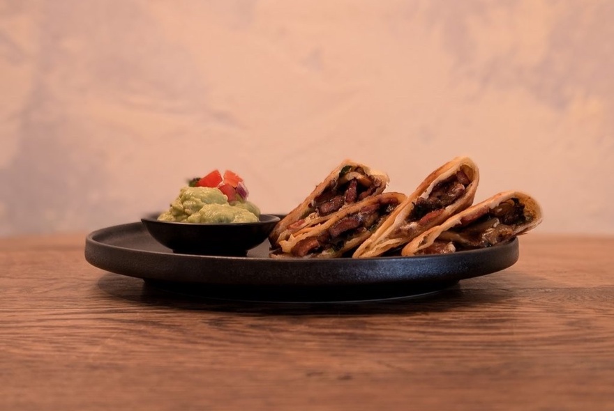 A dish of Mexican tacos with a bowl of guacamole.