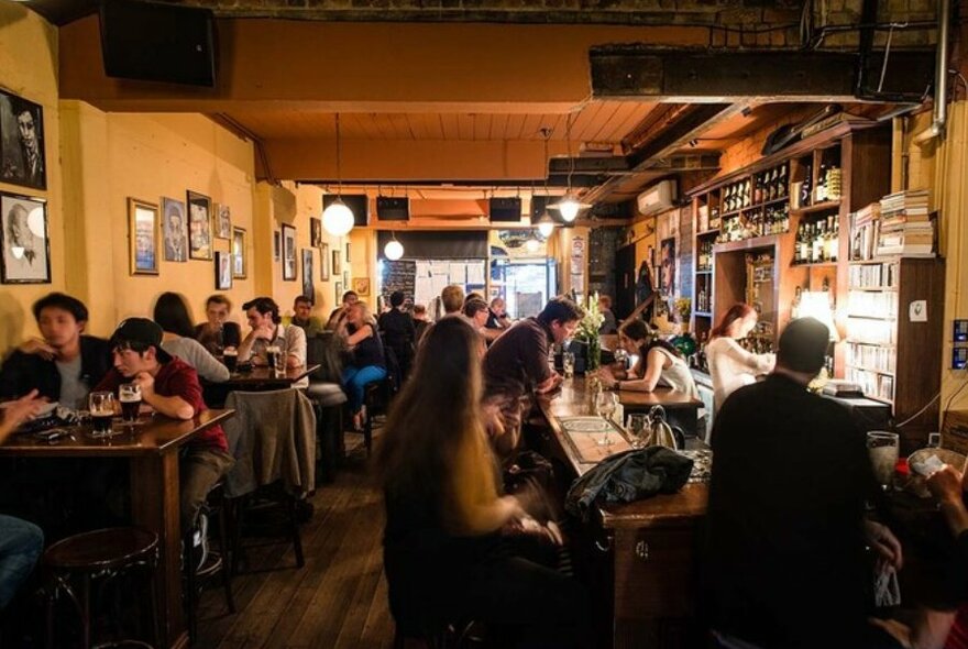 People drinking and seated at small tables, and at the bar, in an Irish pub.