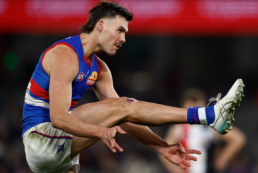 Western Bulldogs AFL football player with his leg raised high in the air, having just kicked the footy.