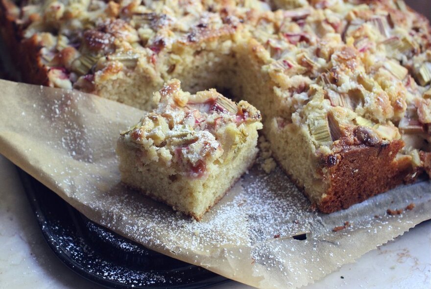 Apple cake dusted with icing sugar on baking paper.