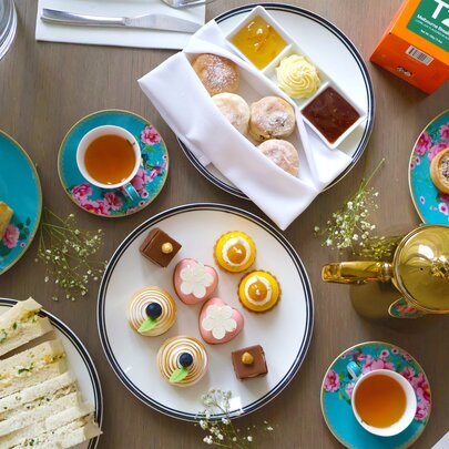A top-down view of a high tea spread featuring a variety of sweet and savoury treats arranged on a wooden table.