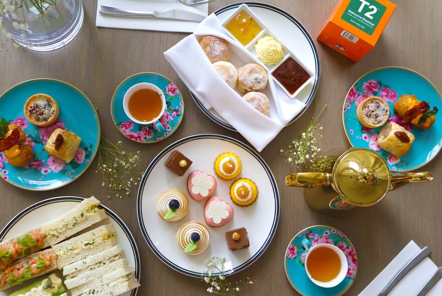 A top-down view of a high tea spread featuring a variety of sweet and savoury treats arranged on a wooden table.