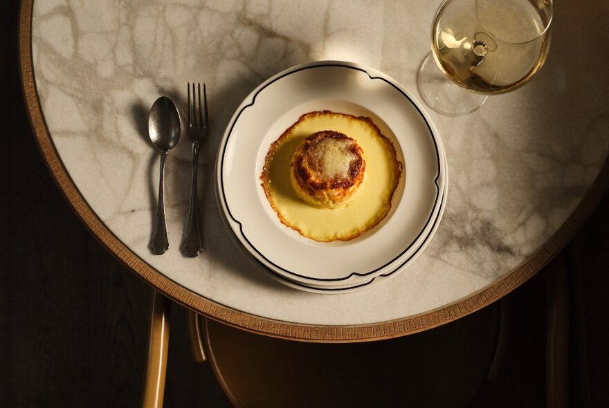 Looking down on a round marble table with a dessert on a plate and a glass of wine. 