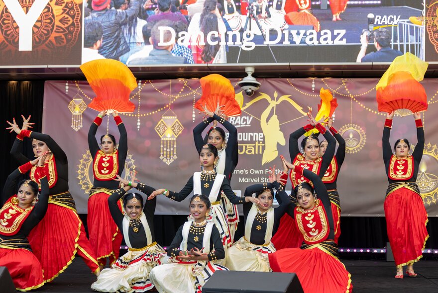Children in traditional dress dancing on a stage in front of signage.
