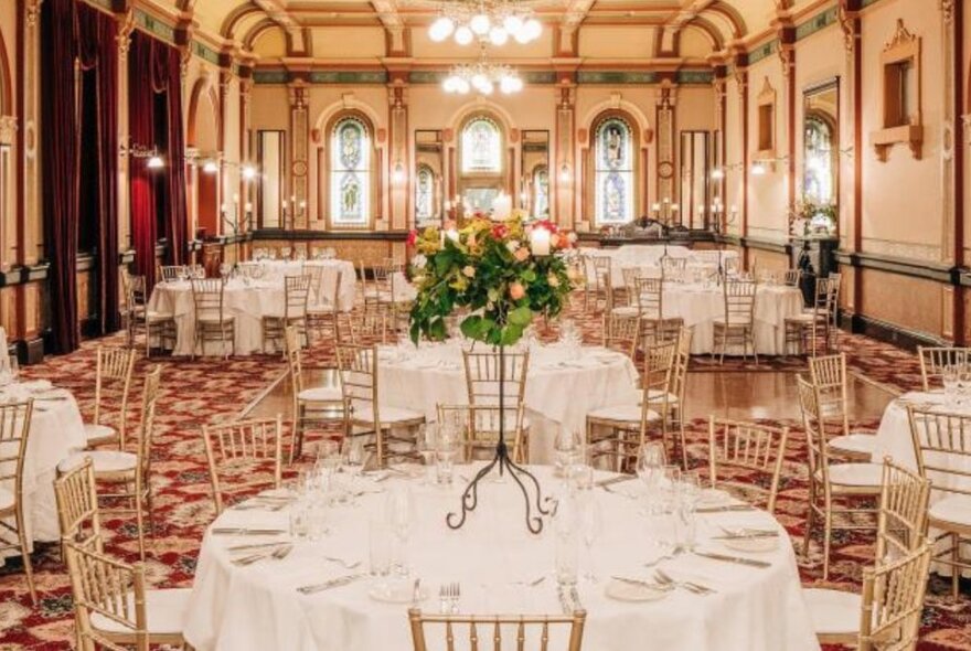 The elegant high-ceilinged Grand Ballroom at the Windsor Hotel, with round tables set for service with white linen, crockery and glassware.