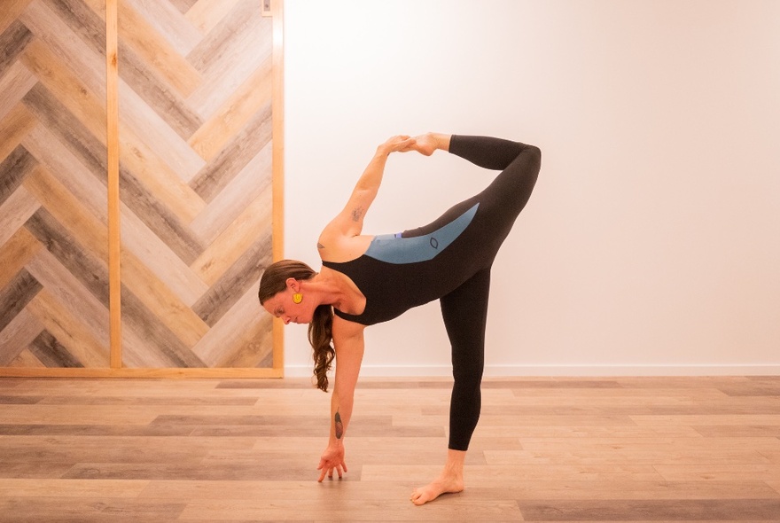 Yoga practitioner practising a pose with leg bent and arms stretching in a room with wooden floors.