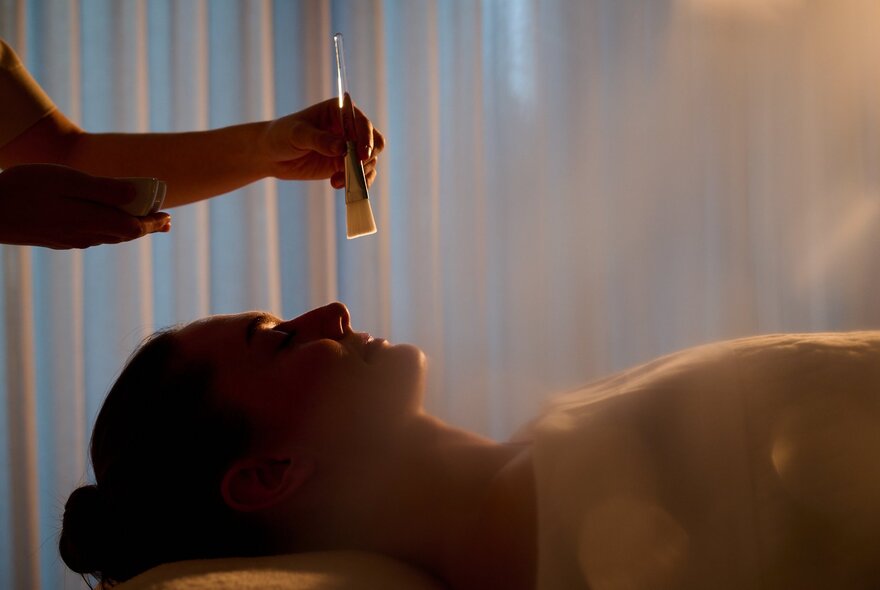 Woman receiving a spa treatment in a dimly lit space with diffused light.
