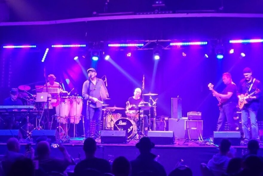 Live rock band playing under lights in a purple-hued venue.