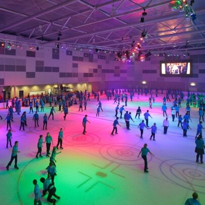 People skating in an indoor ice rink with disco lighting.