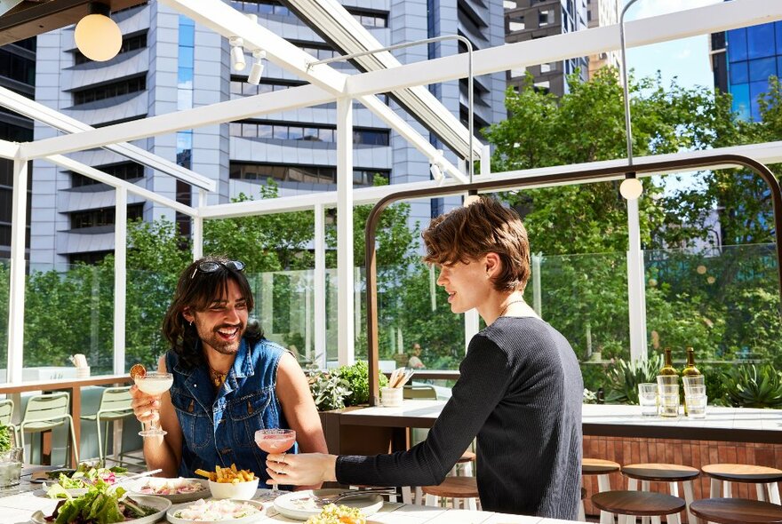 Two people sharing food and drinks on a city rooftop.