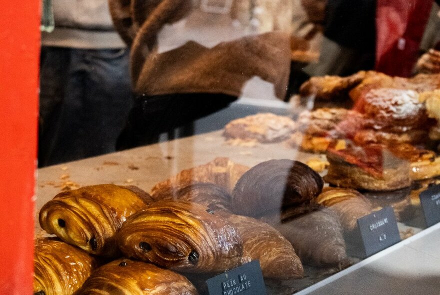 Pastries on a bench behind a bakery window with reflections.