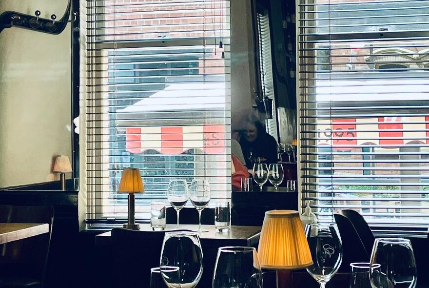 A cosy restaurant bar with table lamps, glasses and venetian blinds.