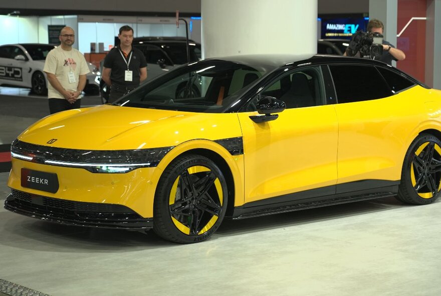 People standing next to a yellow electric vehicle indoors.