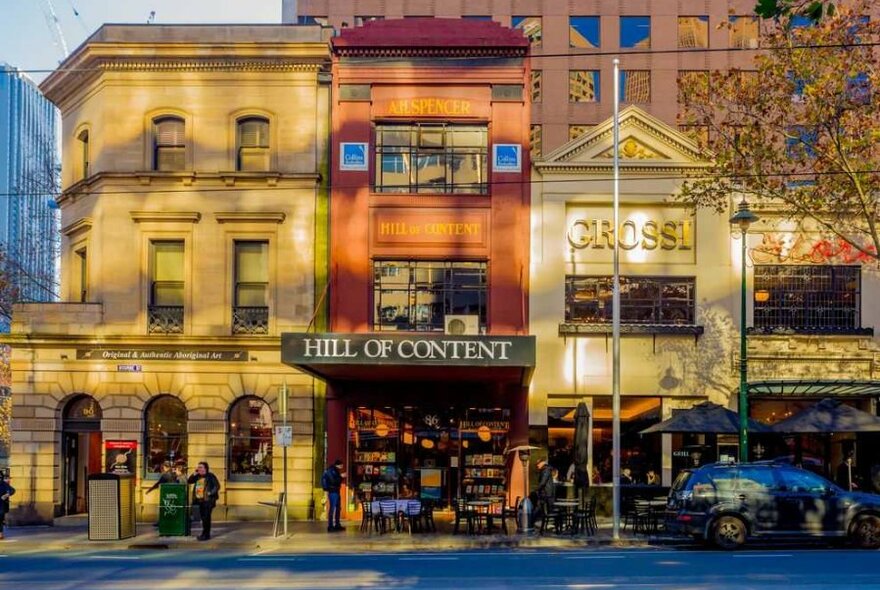 Three tall buildings on a city street that house small shops and restaurants