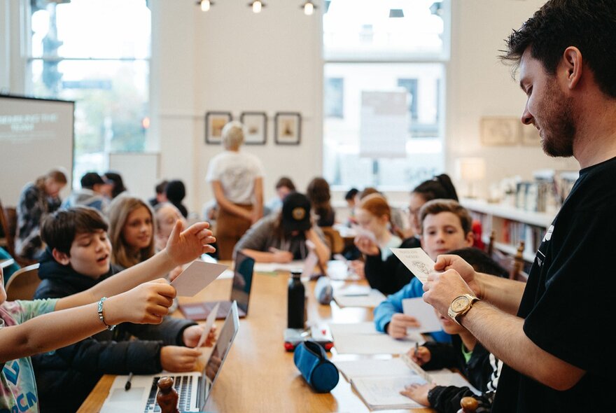 Children working at tables in a workshop setting, hands outstretched to a teacher.