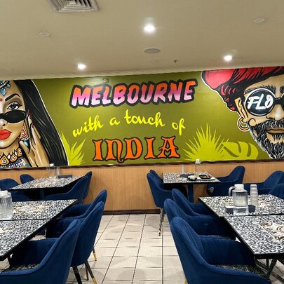 The interior of an Indian Restaurant with a painted mural on the back wall, blue velvet chairs and mosaic tables.