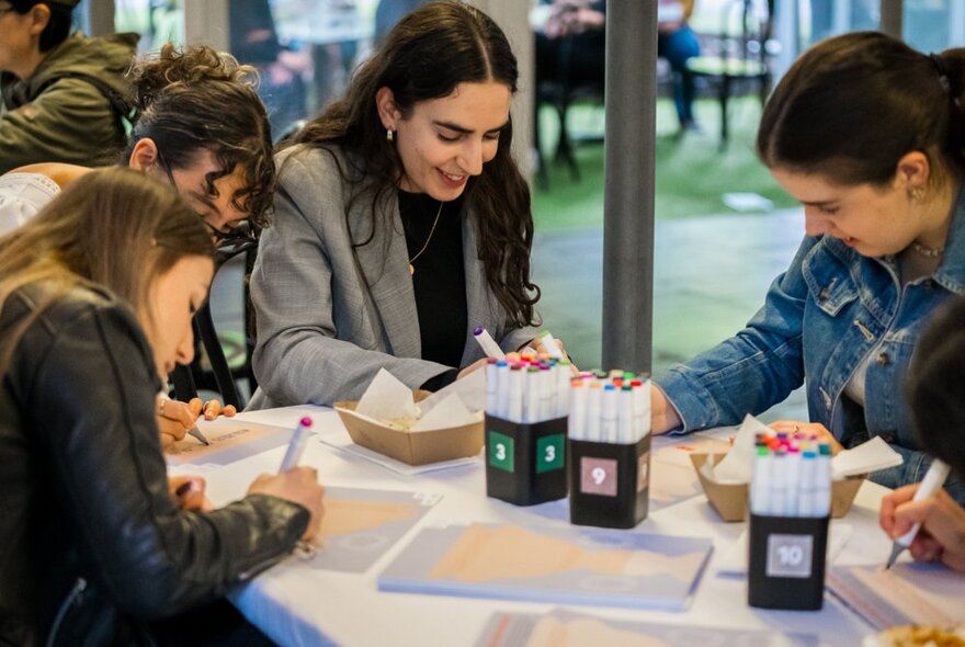 People seated at a table drawing with art materials on the table. 