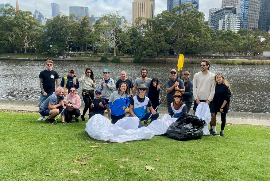 A group of people posing together in front of the Yarra River with rubbish bags and litter grabbers. 