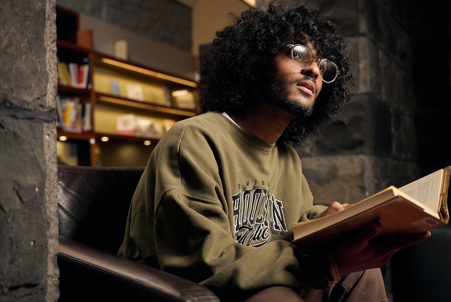 A man with a mop of curly black hair, sitting on a stair reading a book.