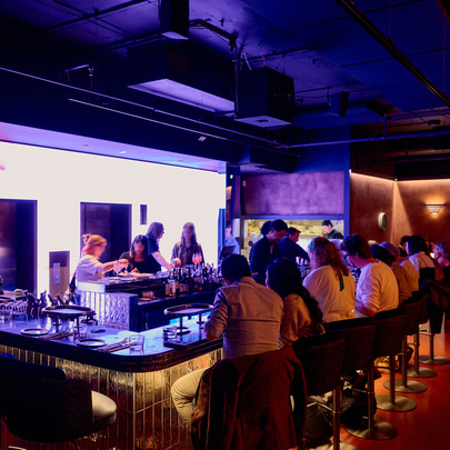 A busy restaurant with people dining and drinking at a bar surrounded by purple neon lights