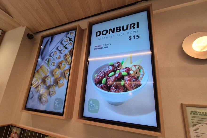 Two digital menu screens fixed to the wall in a small Japanese cafe, showcasing some of the food available.