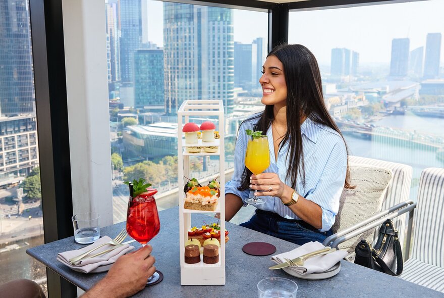 A person is on a rooftop bar sipping cocktails and enjoying high tea. 