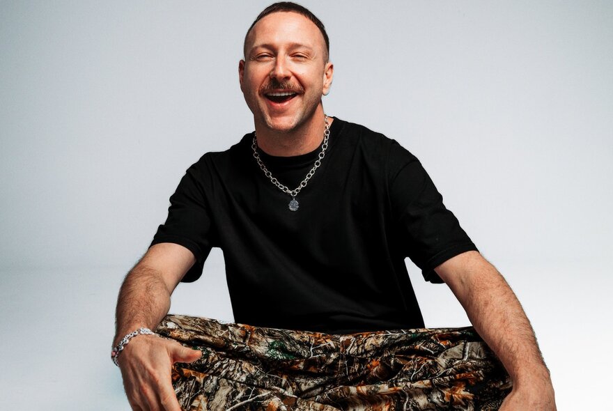 German DJ and electronic music producer Marten Hørger seated and smiling, wearing a black t-shirt and patterned trousers.
