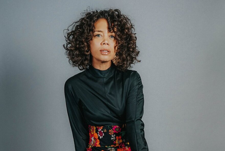 Musician Jade MacRae with short curly hair, wearing a black top and dark flowered skirt.