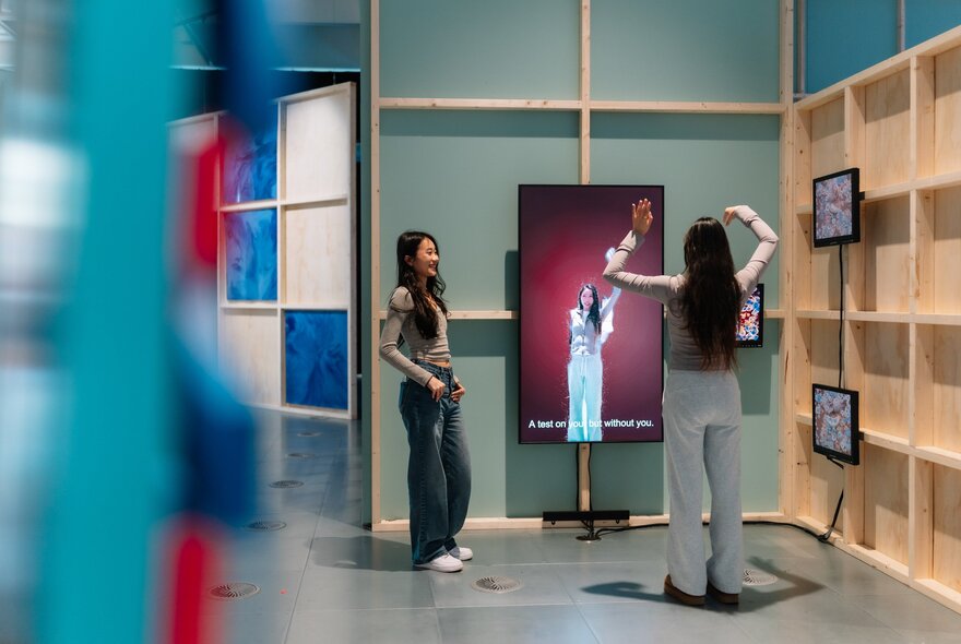 Two young adults exploring a digital display in a gallery space.