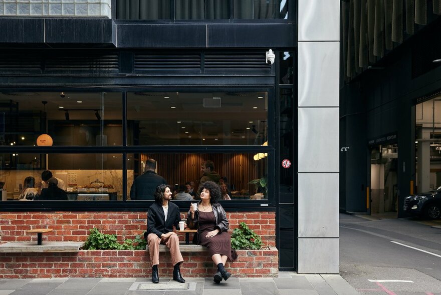 Two friends are sitting outside a cafe drinking coffee