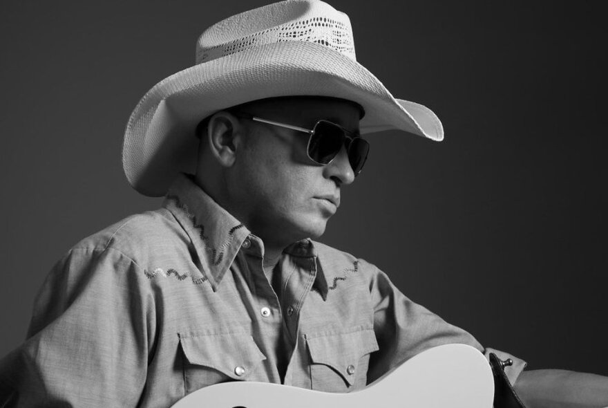 Black and white profile of the musician Diesel, wearing a white cowboy hat and dark sunglasses, with the top of his guitar just in the frame.