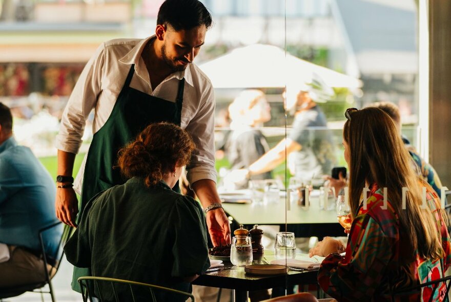 A waiter presenting a plate to two diners.