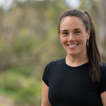 Smiling woman dressed in black T-shirt, standing in front of blurred garden background.