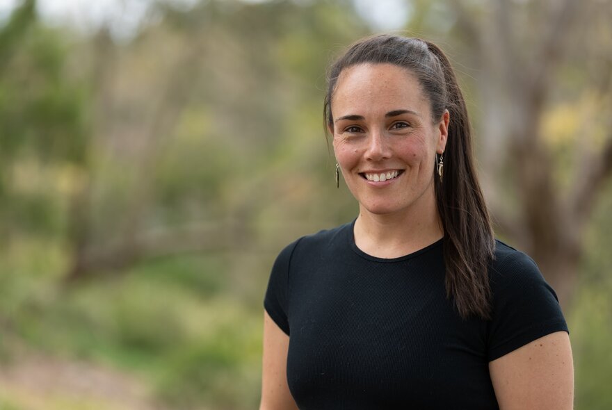 Smiling woman dressed in black T-shirt, standing in front of blurred garden background.