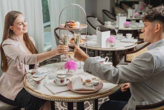 A couple touching glasses over a table set with an elaborate afternoon tea.