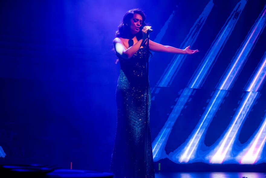 A cabaret singer on stage with a long dress and arm outstretched. 