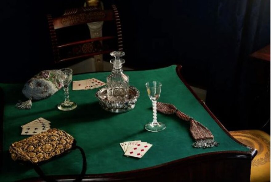 Green baize card table set with playing cards, Georgian wine glasses and decanter.