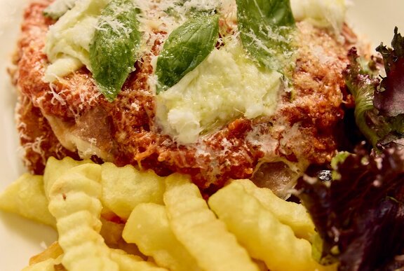 Close-up of chicken parma with salad and chips, on a plate.