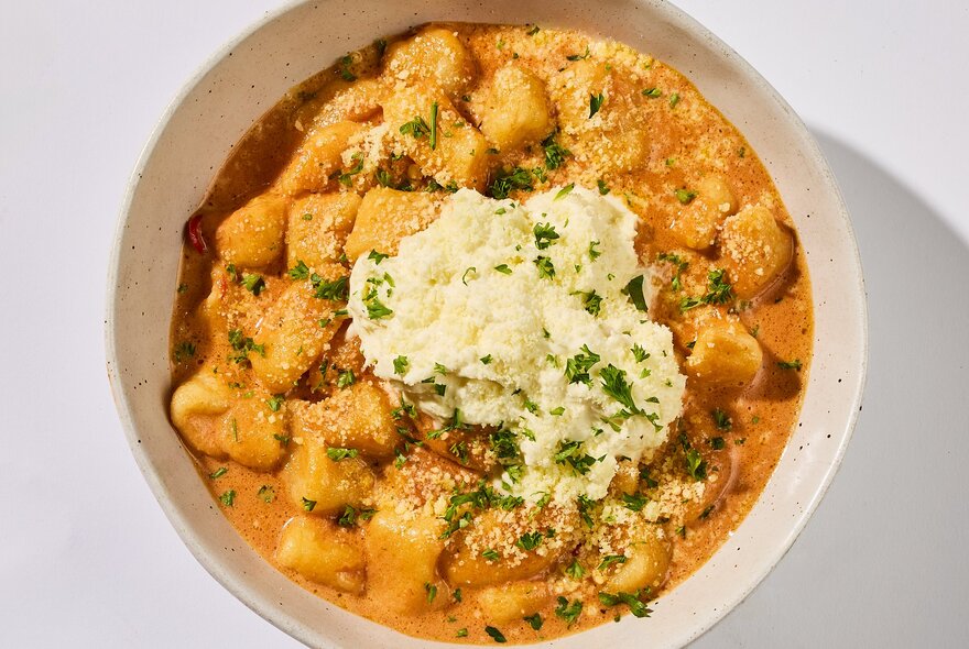 A bowl of pumpkin gnocci, seen from above, with grated parmesan on top.