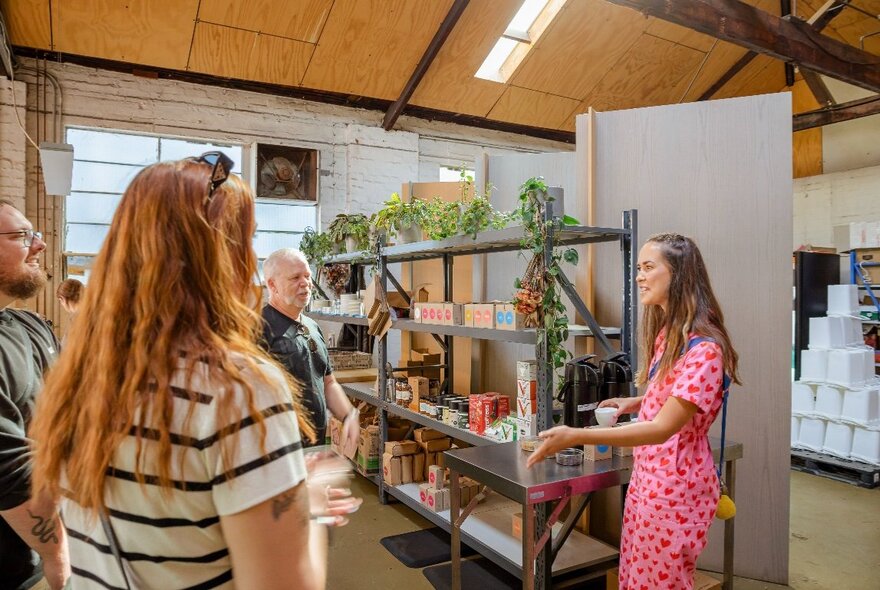 A tour guide talking to a group of people inside a coffee roasters, with a shelf of products on display.