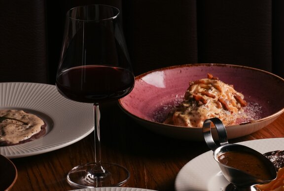 Plates of food and a glass of red wine on a table.
