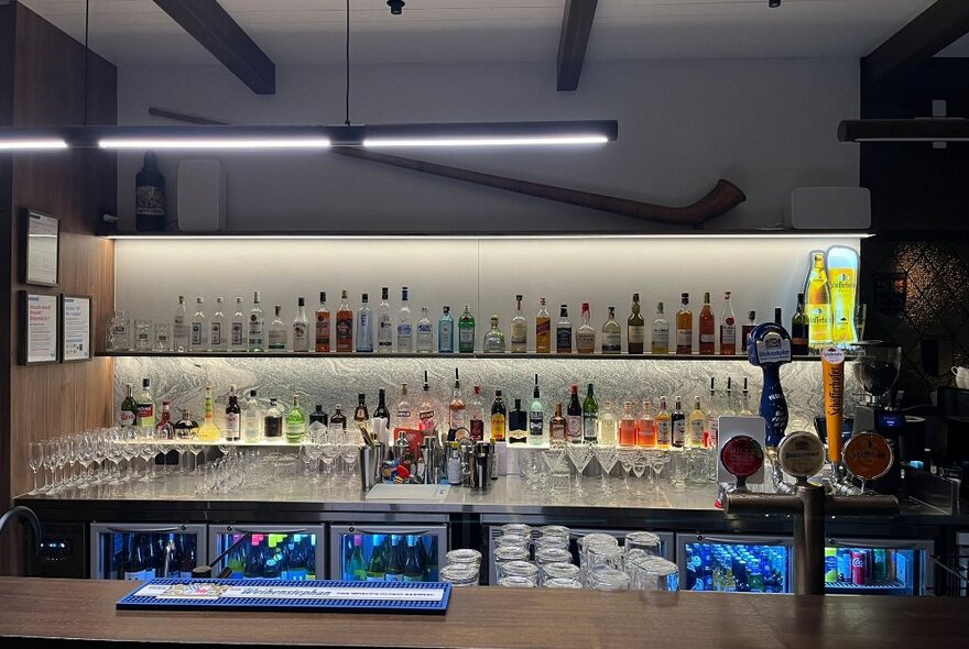 The bar at a restaurant, with blue-lit lower fridges and a white shelf with spirits of all kinds displayed.