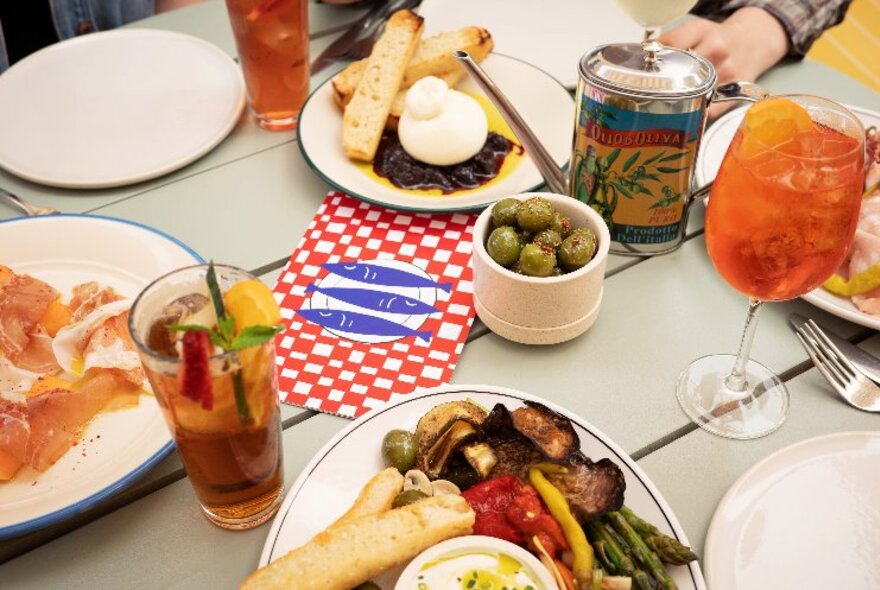 Spritz cocktails on a table with antipasto, olives, salumi and other snacks.