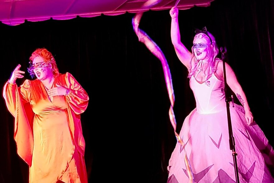 Performers on stage in flowing dresses with stage makeup and coloured lights. 