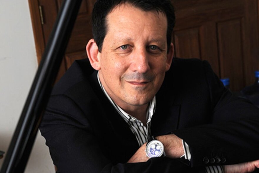 Musician Jeff Lorber close up with his arms folded in front of his chest, wearing a dark suit jacket and gazing directly ahead.