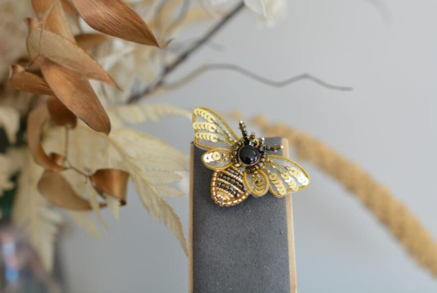 A small wodden display showcasing an embroidered bee.