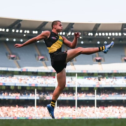 Richmond AFL football player kicking in midair during a game.