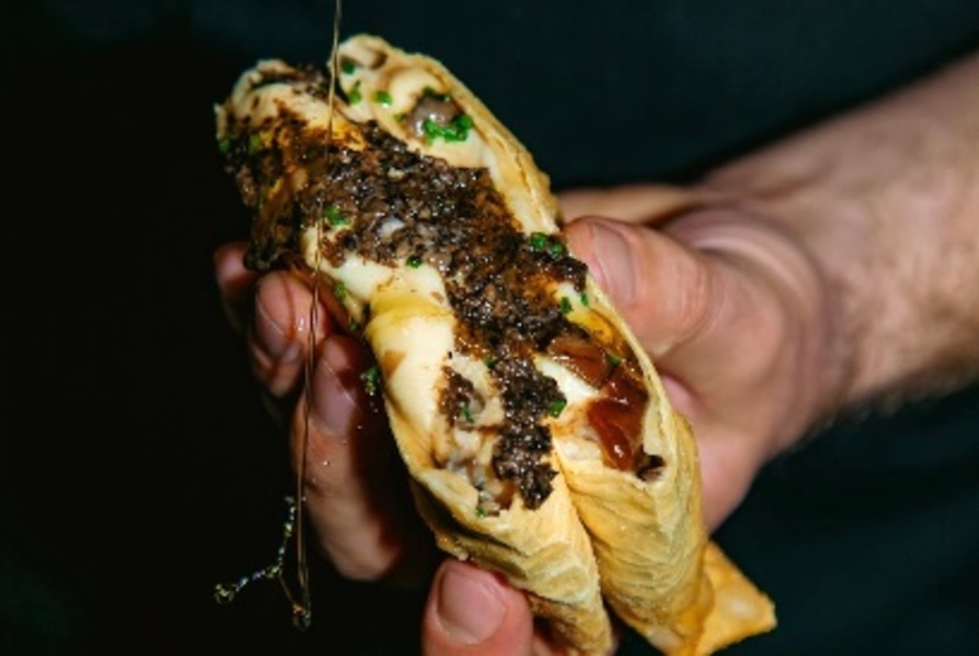 Hand holding a deep fried lasagne pocket cut in half to reveal the contents