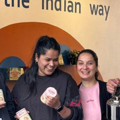 Four people laughing and posing with various chai cannisters and teapots.