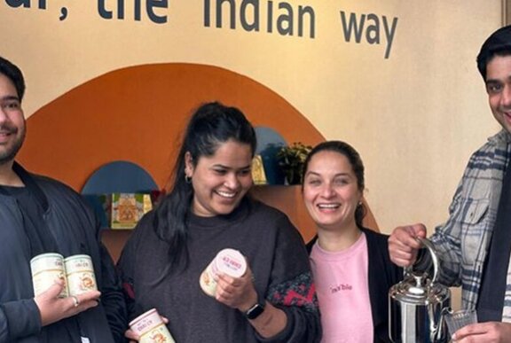 Four people laughing and posing with various chai cannisters and teapots.